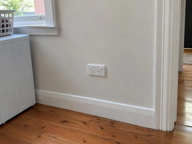 Double power point on a painted wall beside timber floorboards and a doorway in Coogee