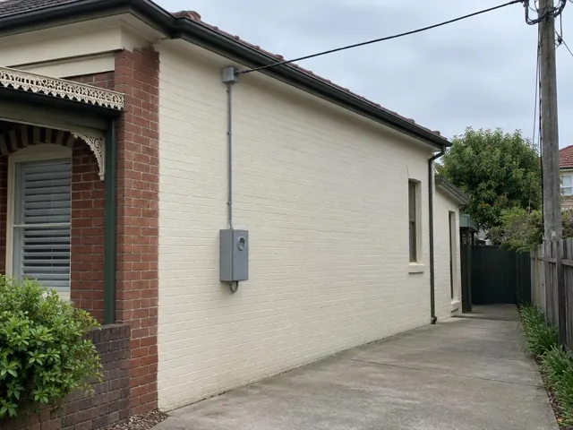 Cream brick house with overhead service cable and grey point-of-attachment bracket on the side wall in Kingsford