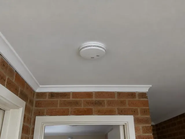 Ceiling-mounted smoke alarm above a brick interior doorway in a home in Matraville